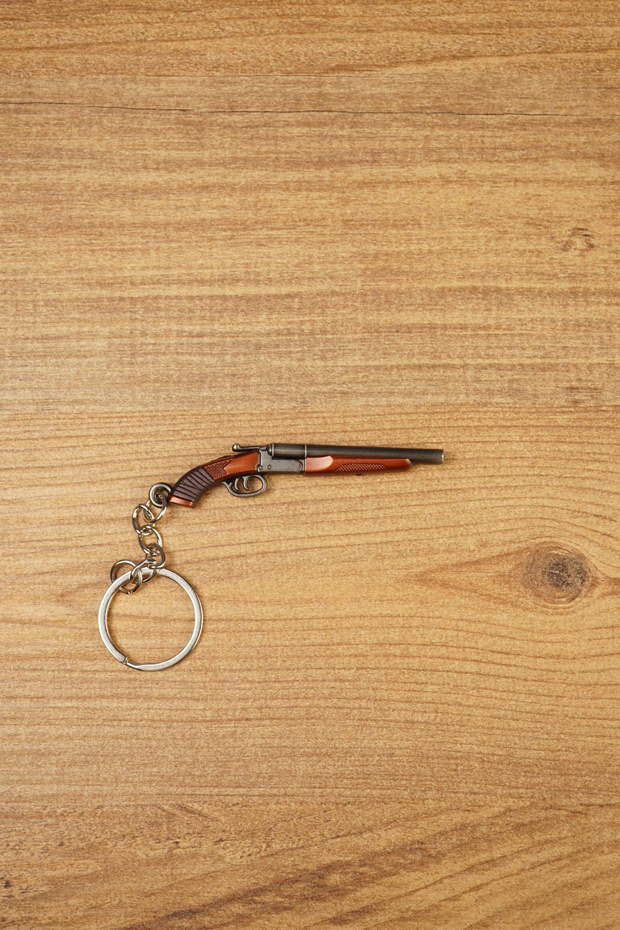 12GA double-barrel shotgun keychain lying flat on a wooden surface, showing the mini gamer replica with metal keyring attachment