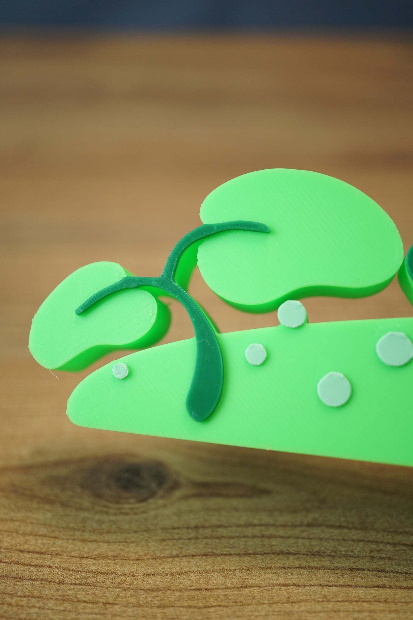 Close-up of the leafy end of the Palia New in Town nameplate with green plant accents and small pale dot details on the sign base.