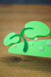 Close-up of the leafy end of the Palia New in Town nameplate with green plant accents and small pale dot details on the sign base.
