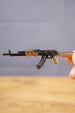 Close-up of AK-74 rifle keyring held by hand, showing detailed black barrel, curved magazine and wood-effect stock finish