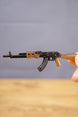 Close-up of AK-74 rifle keyring held by hand, showing detailed black barrel, curved magazine and wood-effect stock finish
