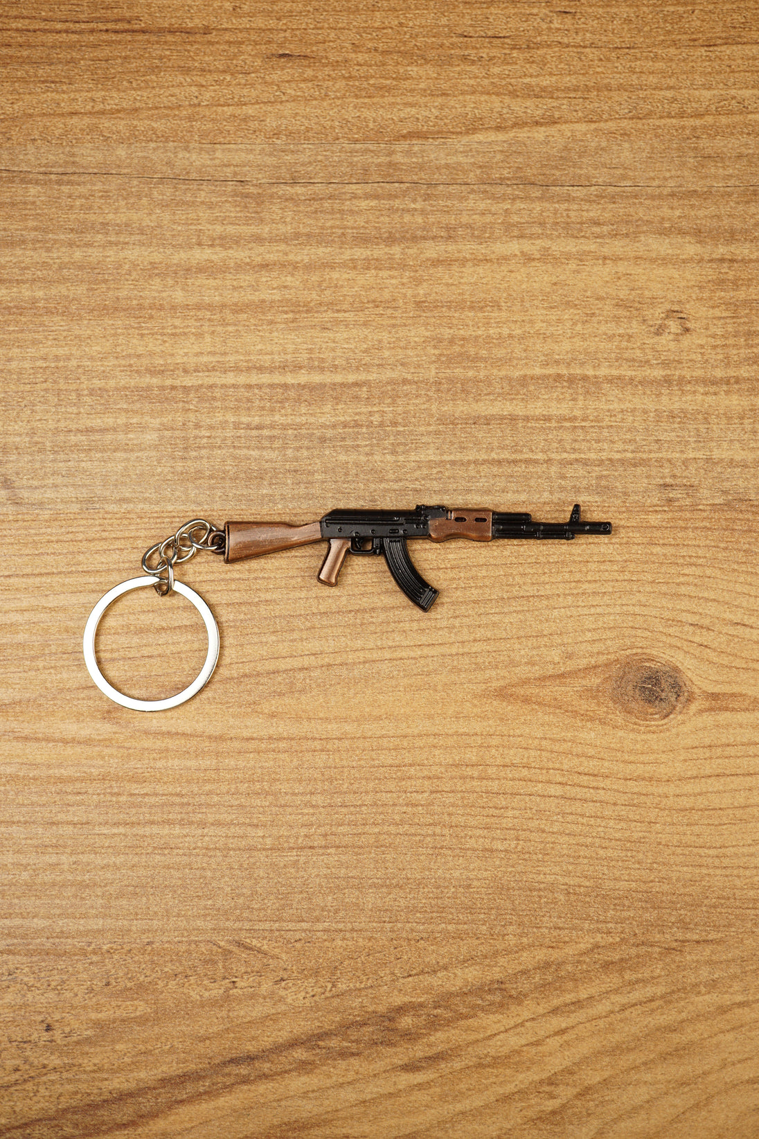 AK-74 rifle keyring laid flat on wooden surface with metal key loop, ideal tactical FPS gamer gift and collectible bag charm