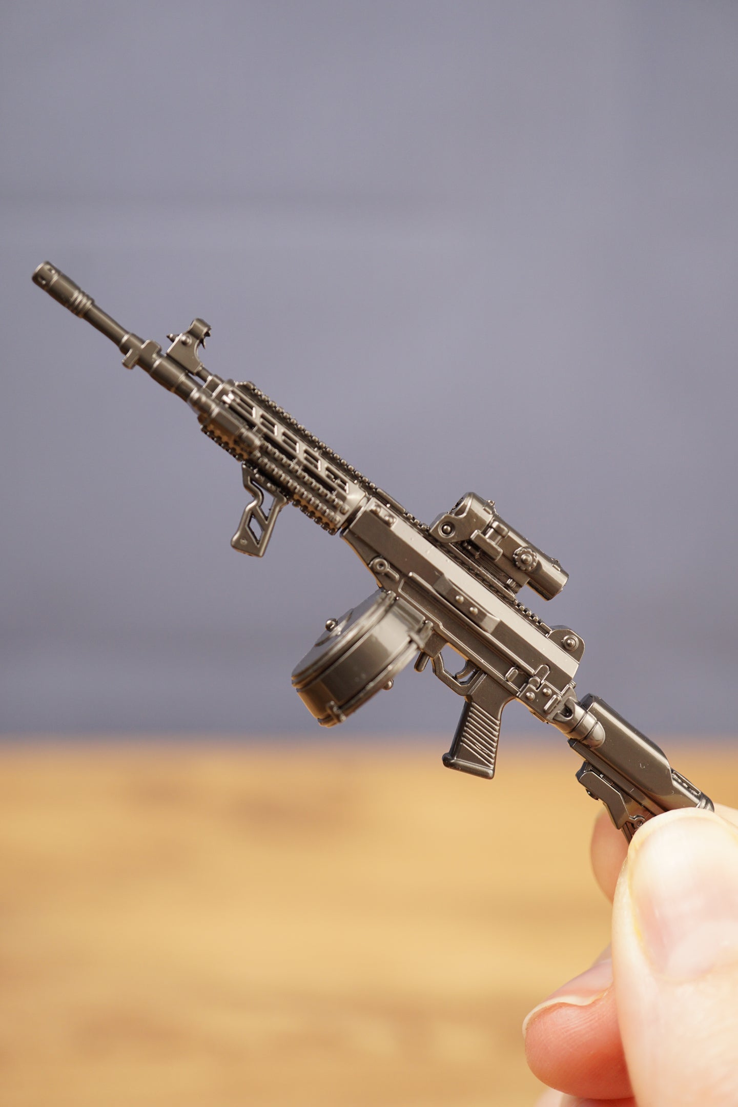 Hand holding AK-12 rifle keychain with drum magazine, showing scale and fine detailing for FPS fans and military collectors