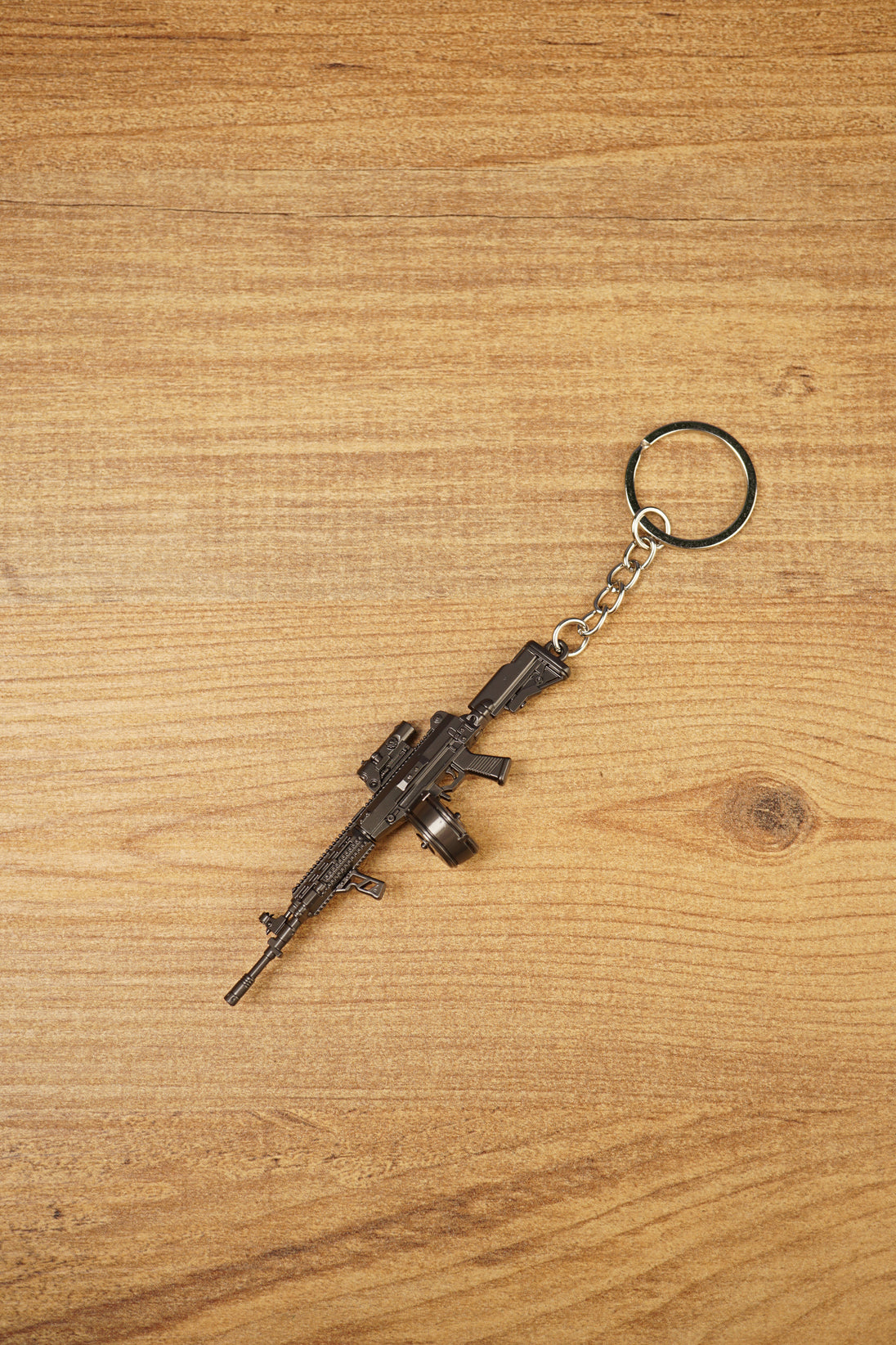 Detailed AK-12 style rifle keychain with drum mag laid flat on wood, ideal as a tactical FPS gamer gift or bag charm