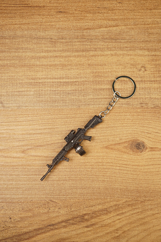 Detailed AK-12 style rifle keychain with drum mag laid flat on wood, ideal as a tactical FPS gamer gift or bag charm