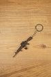 Detailed AK-12 style rifle keychain with drum mag laid flat on wood, ideal as a tactical FPS gamer gift or bag charm