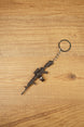 Detailed AK-12 style rifle keychain with drum mag laid flat on wood, ideal as a tactical FPS gamer gift or bag charm