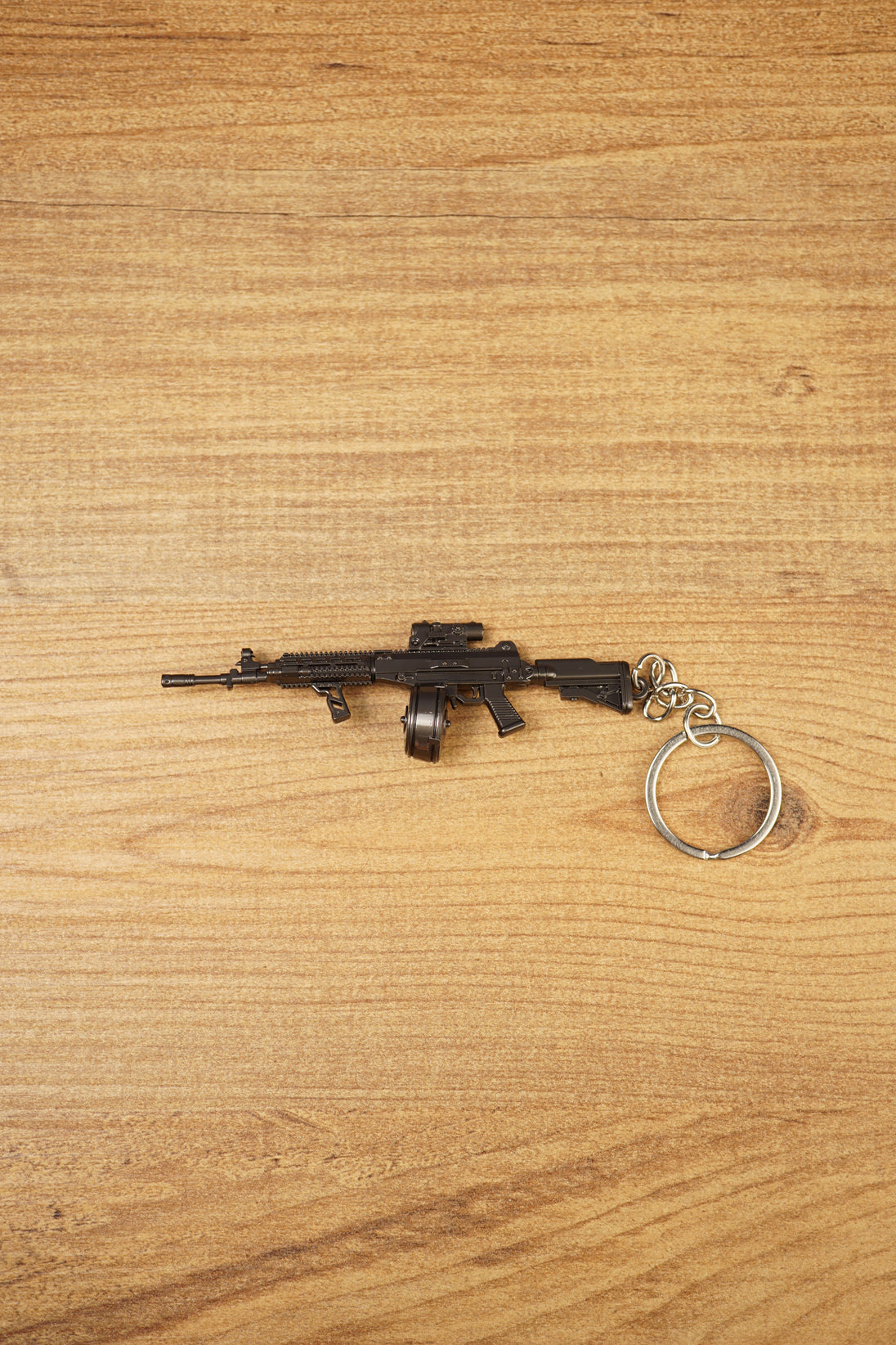 AK-12 rifle keyring with drum magazine on a wooden surface, showing the full metal gamer collectible with chain and ring attached