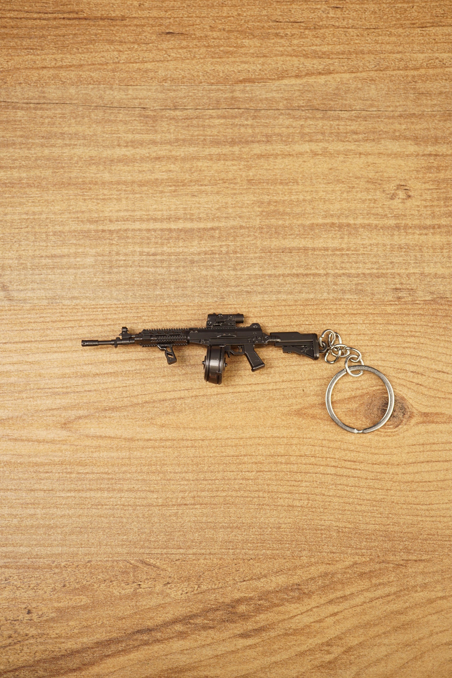 AK-12 rifle keyring with drum magazine on a wooden surface, showing the full metal gamer collectible with chain and ring attached