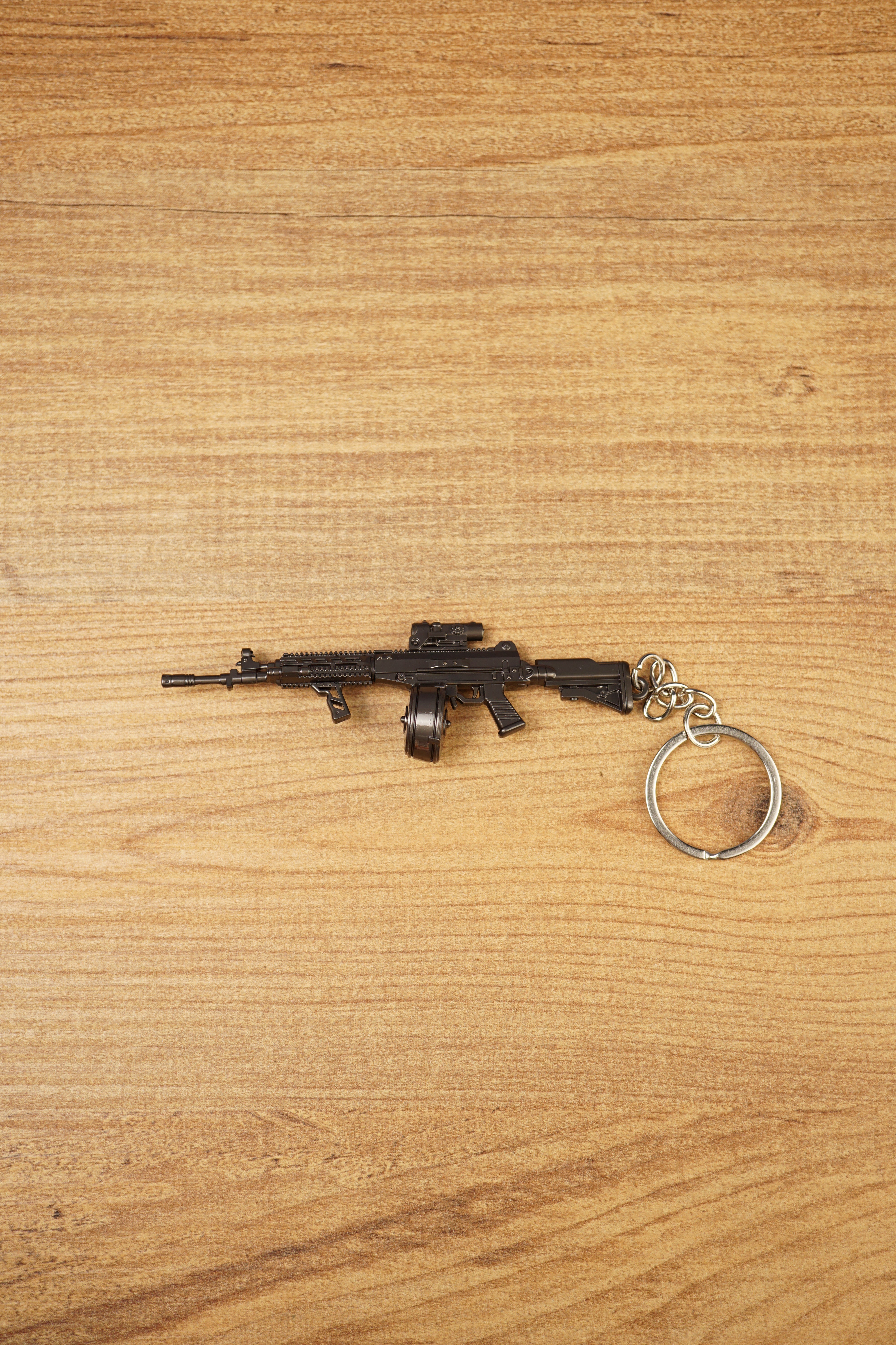 AK-12 rifle keyring with drum magazine on a wooden surface, showing the full metal gamer collectible with chain and ring attached