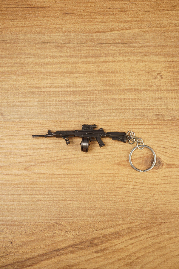 AK-12 rifle keyring with drum magazine on a wooden surface, showing the full metal gamer collectible with chain and ring attached