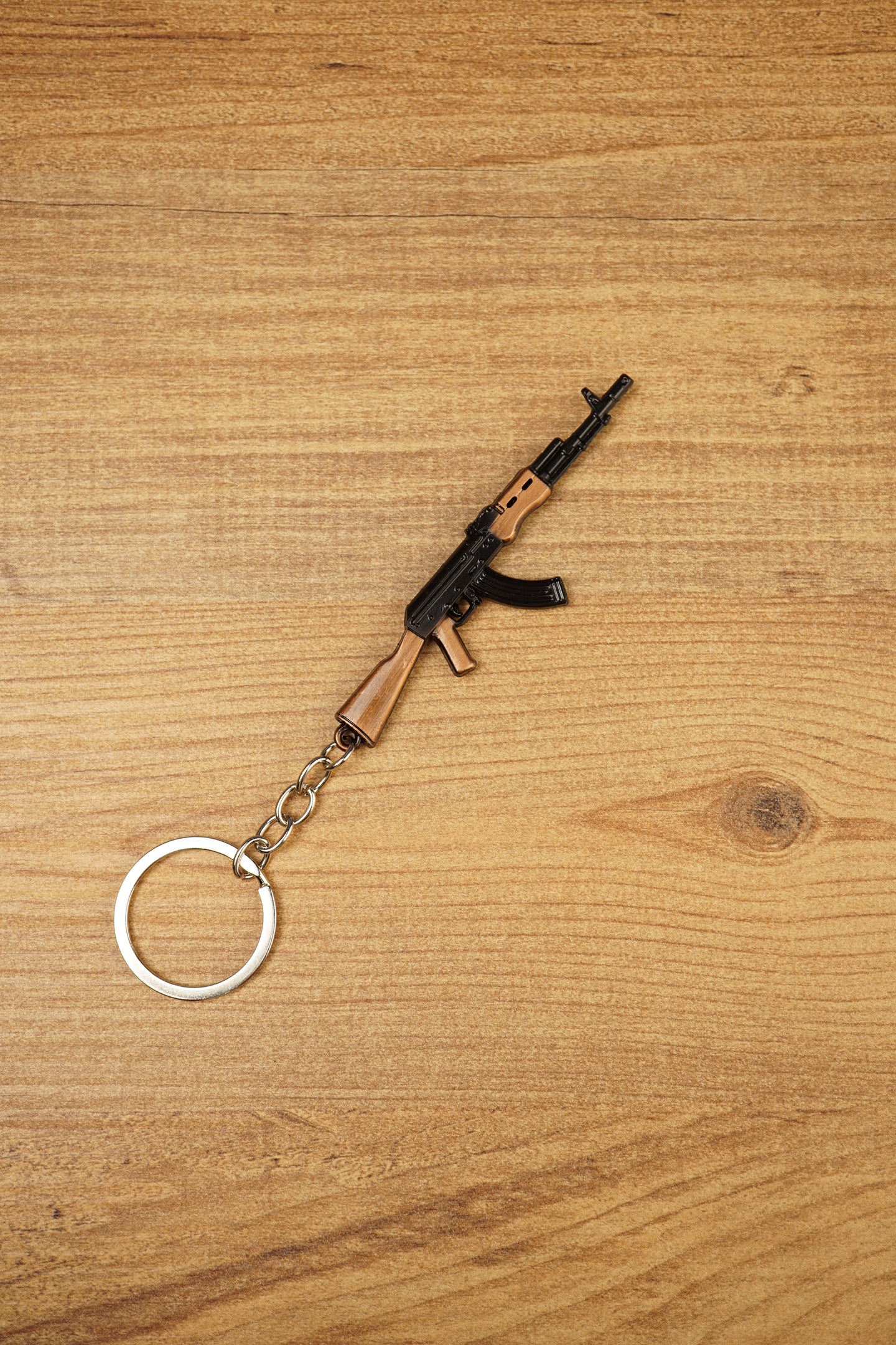 Miniature AK-74 rifle keyring angled on wood background, showing curved magazine, black body and wood-effect rifle details