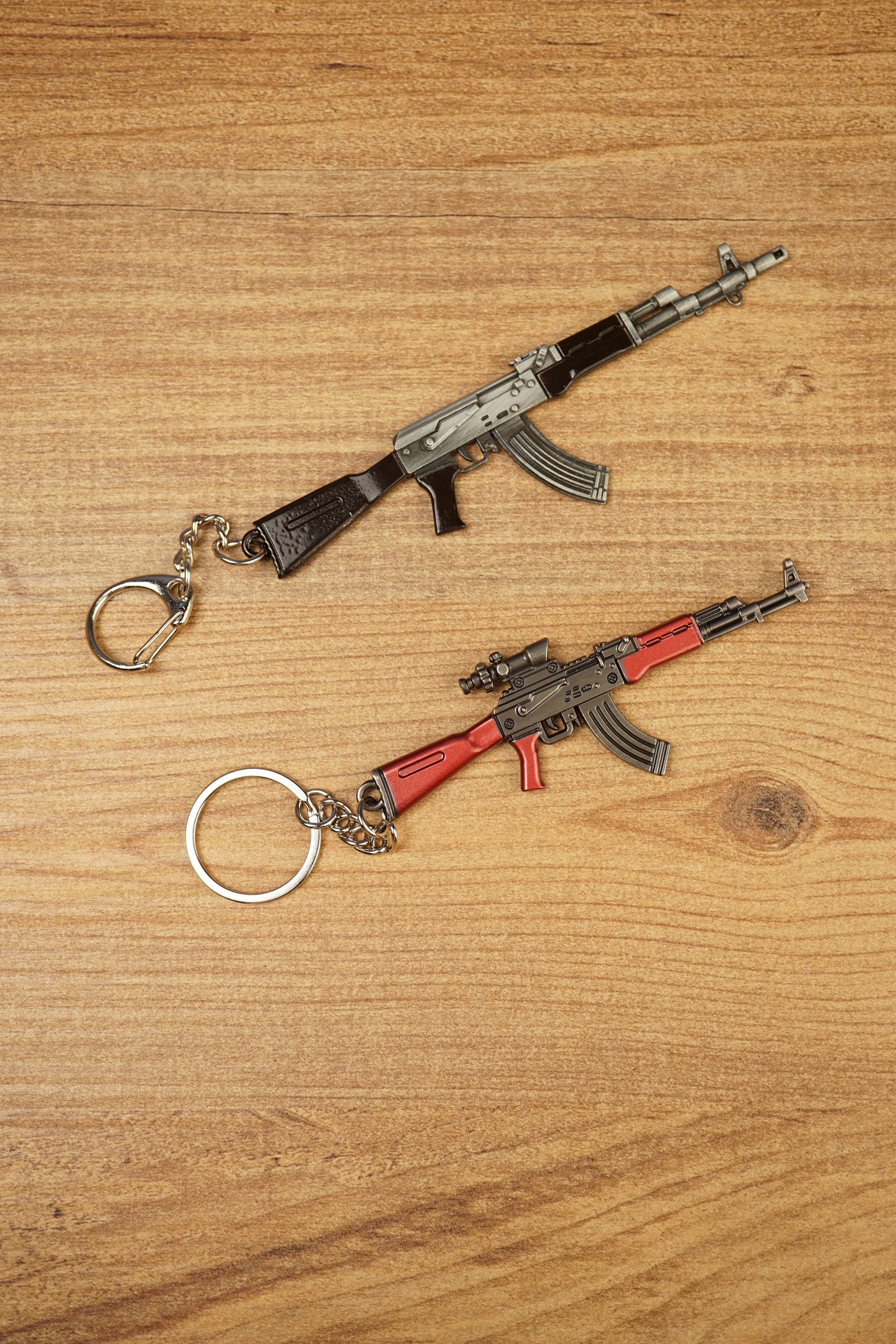 Base black AKM rifle keychain and red modded rifle keyring displayed diagonally on wood with detailed miniature parts visible