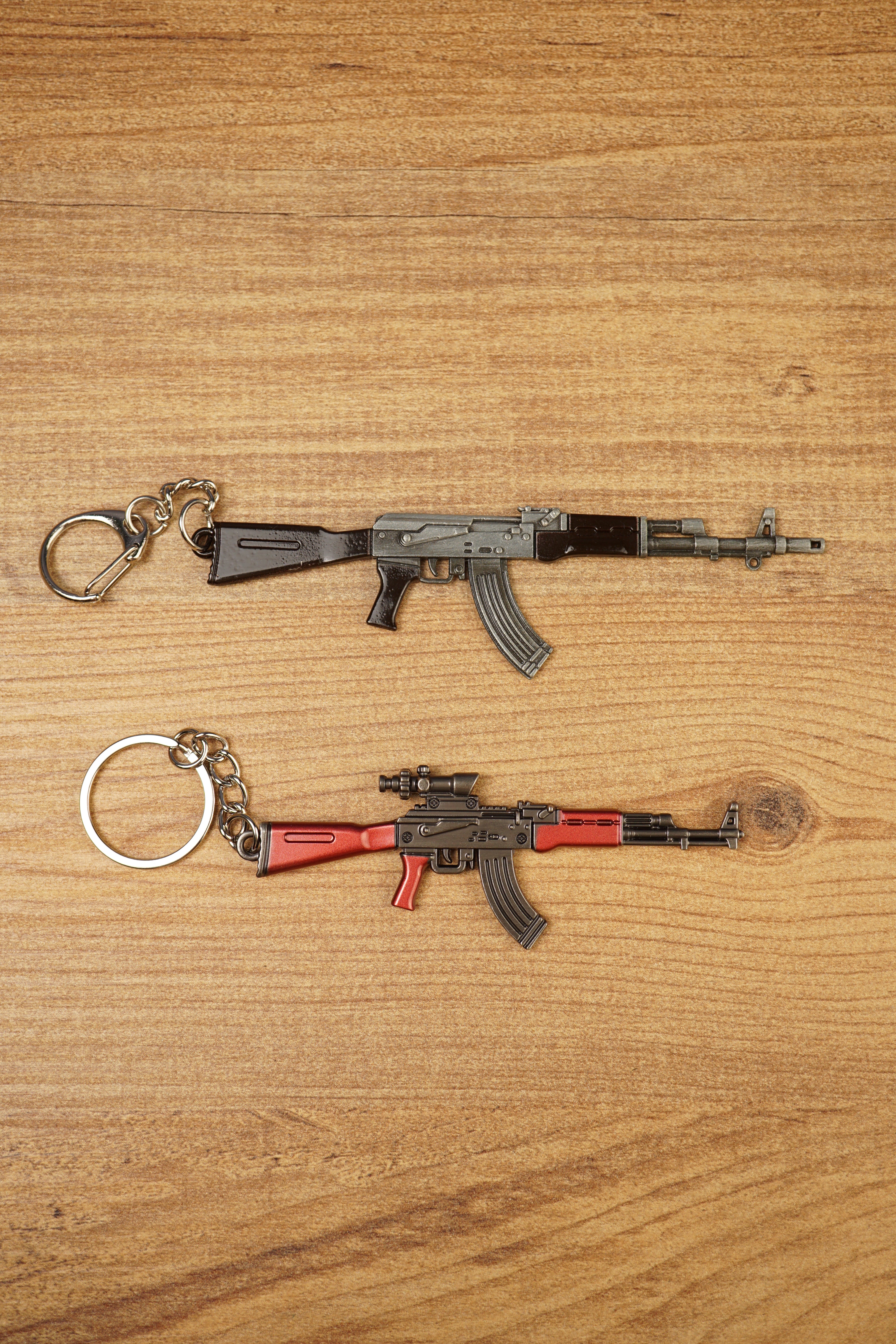 AKM 7.62x39 rifle keychain replicas in base and red modded styles laid flat on a wooden surface for tactical gamer collectors