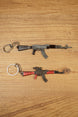 AKM 7.62x39 rifle keychain replicas in base and red modded styles laid flat on a wooden surface for tactical gamer collectors