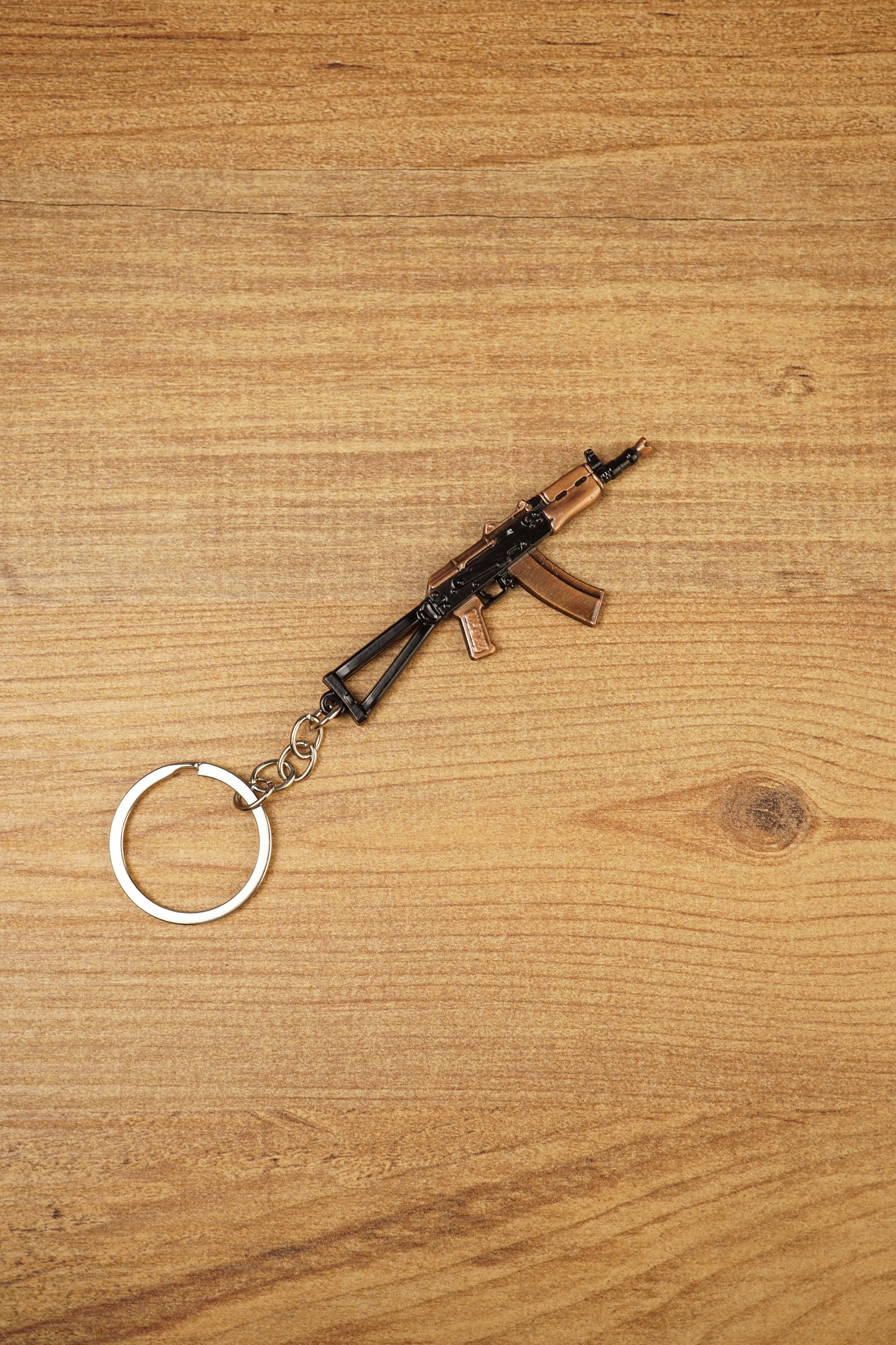 Angled AKS-74U rifle keyring on wood, a metal FPS gamer accessory with folding stock detail, curved magazine and silver keyring loop