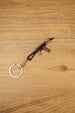 Angled AKS-74U rifle keyring on wood, a metal FPS gamer accessory with folding stock detail, curved magazine and silver keyring loop