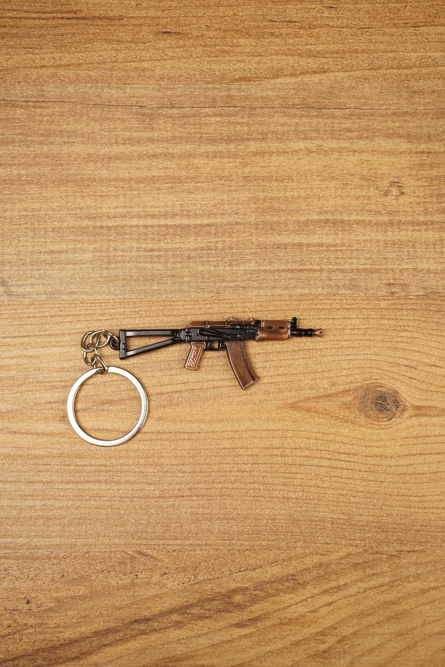 AKS-74U rifle keyring laid flat on a wooden surface, showing the compact metal gamer keychain with bronze and black tactical detailing