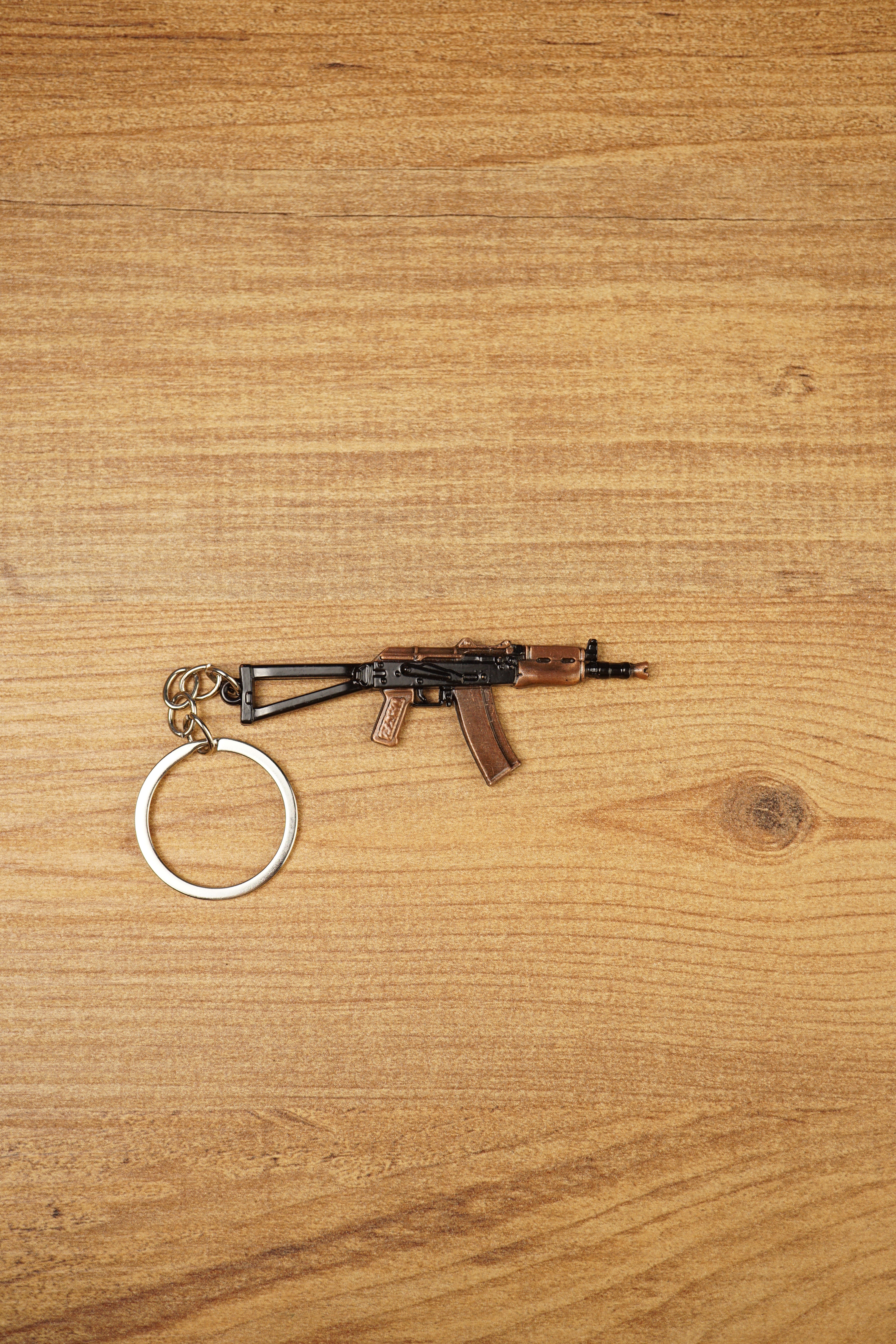 AKS-74U rifle keyring laid flat on a wooden surface, showing the compact metal gamer keychain with bronze and black tactical detailing