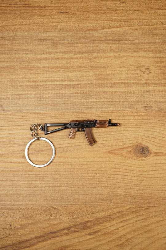 AKS-74U rifle keyring laid flat on a wooden surface, showing the compact metal gamer keychain with bronze and black tactical detailing