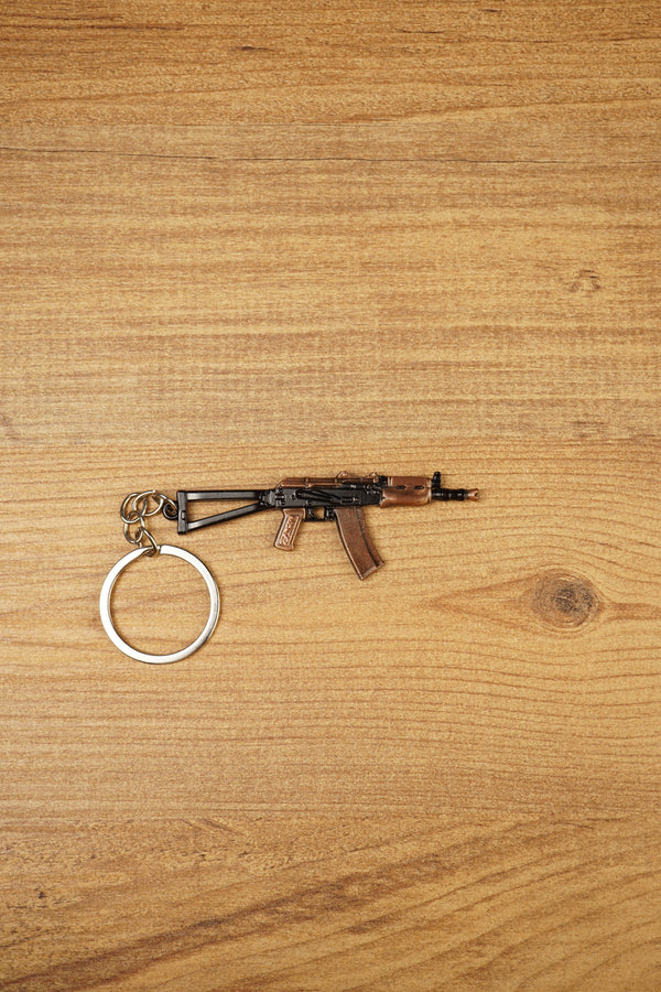 AKS-74U rifle keyring laid flat on a wooden surface, showing the compact metal gamer keychain with bronze and black tactical detailing
