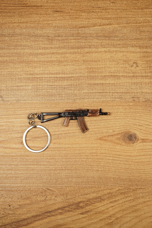 AKS-74U rifle keyring laid flat on a wooden surface, showing the compact metal gamer keychain with bronze and black tactical detailing