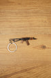 AKS-74U rifle keyring laid flat on a wooden surface, showing the compact metal gamer keychain with bronze and black tactical detailing