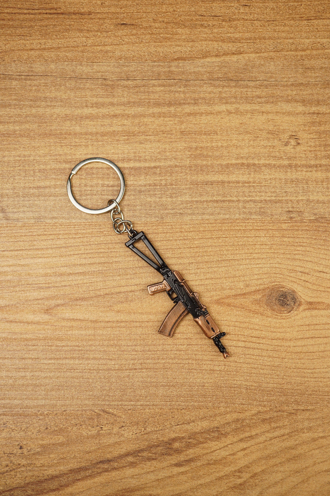 AKS-74U metal rifle keychain displayed vertically on a wooden background, ideal as a tactical gaming gift or backpack charm