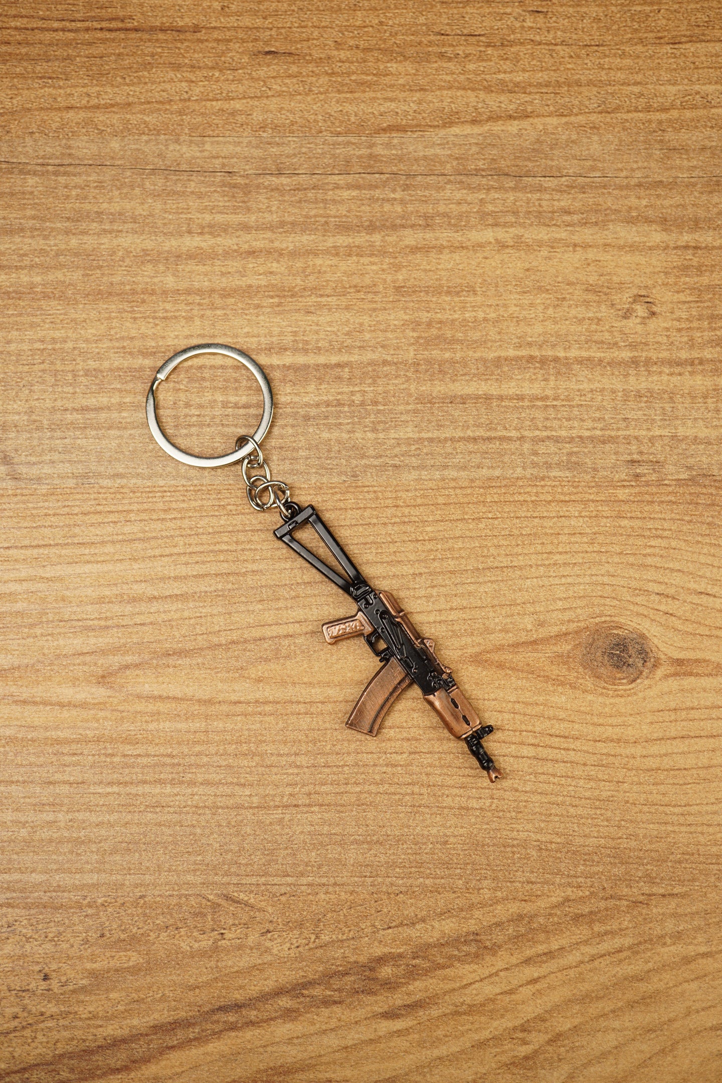 AKS-74U metal rifle keychain displayed vertically on a wooden background, ideal as a tactical gaming gift or backpack charm