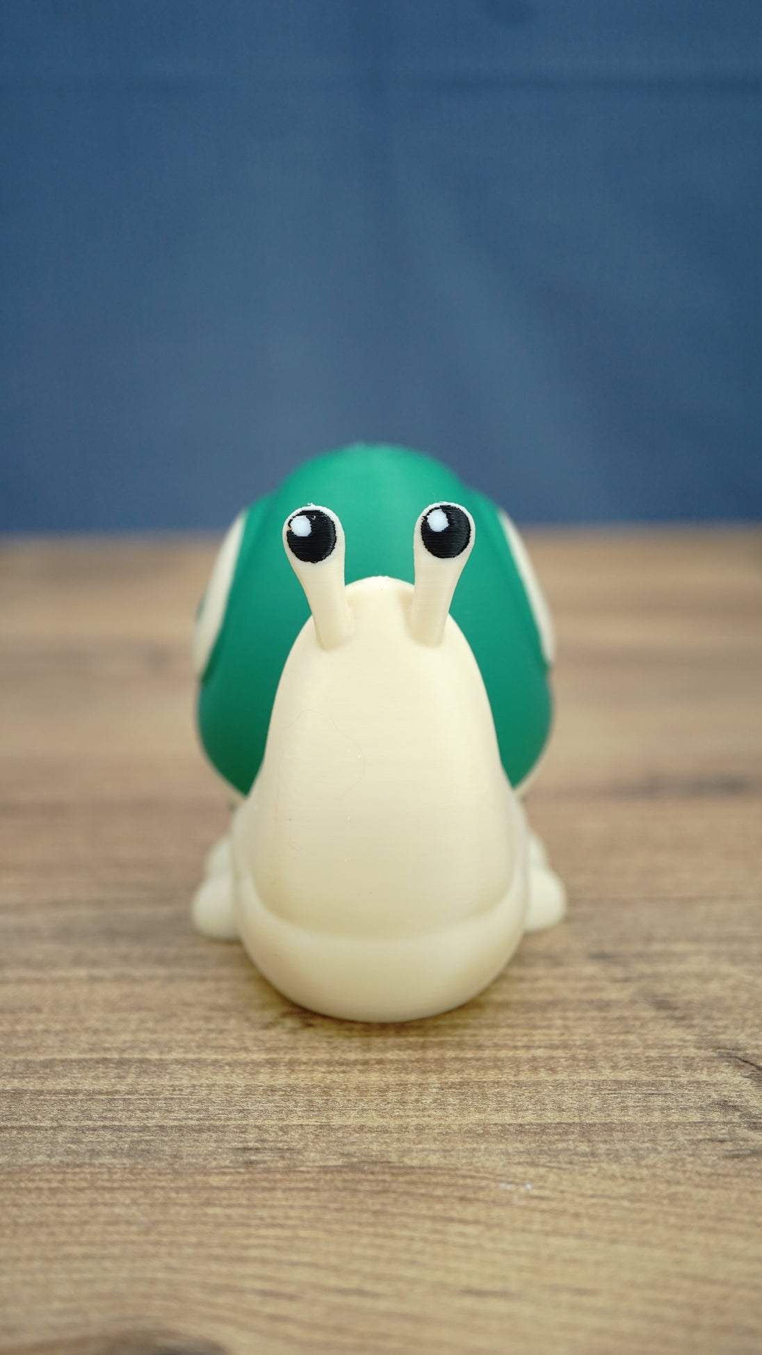 Front view of the Palia Garden Snail Plush collectible figure with a cream-colored body, bright green shell and two expressive black and white eyes
