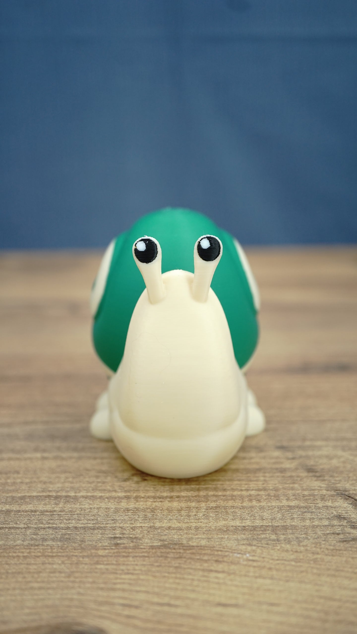 Front view of the Palia Garden Snail Plush collectible figure with a cream-colored body, bright green shell and two expressive black and white eyes