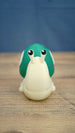 Front view of the Palia Garden Snail Plush collectible figure with a cream-colored body, bright green shell and two expressive black and white eyes