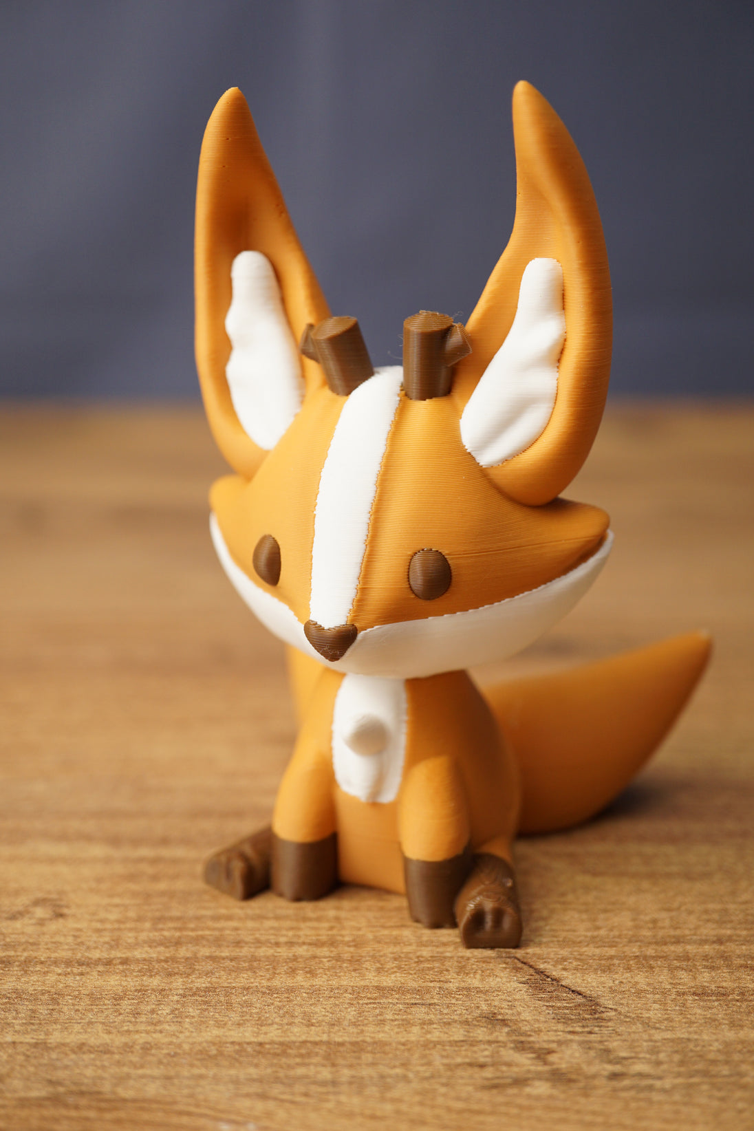 Close-up of Ancient Kitsuu fox figure with orange face, white stripe, brown eyes and antler details on wooden background