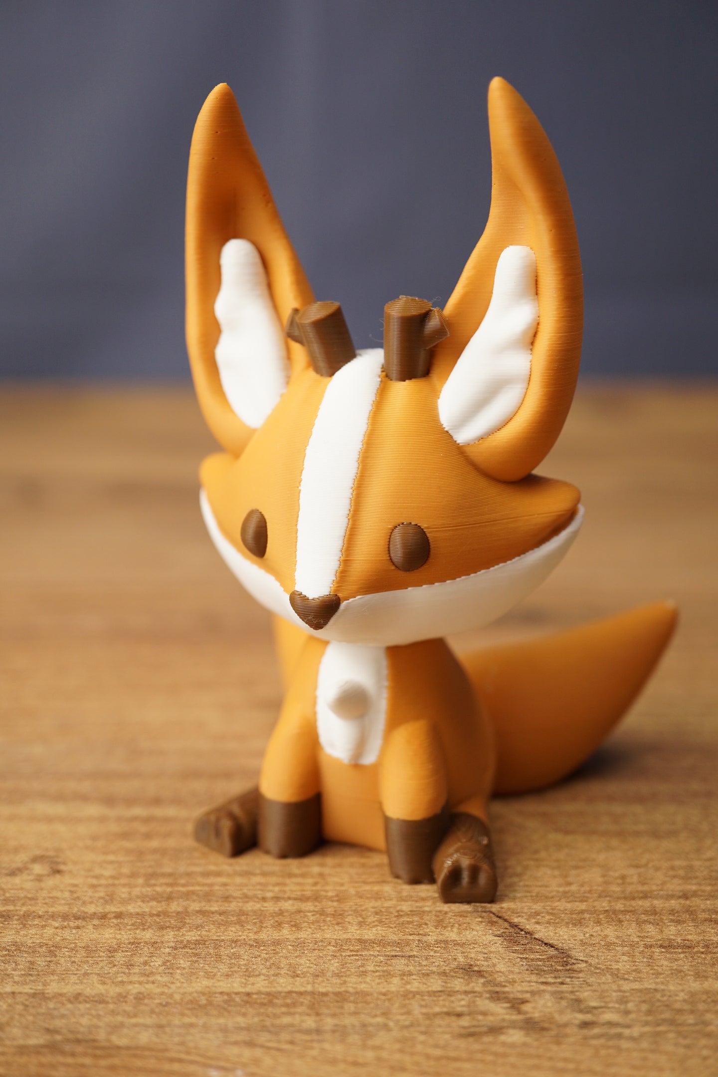 Close-up of Ancient Kitsuu fox figure with orange face, white stripe, brown eyes and antler details on wooden background
