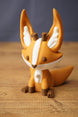 Close-up of Ancient Kitsuu fox figure with orange face, white stripe, brown eyes and antler details on wooden background