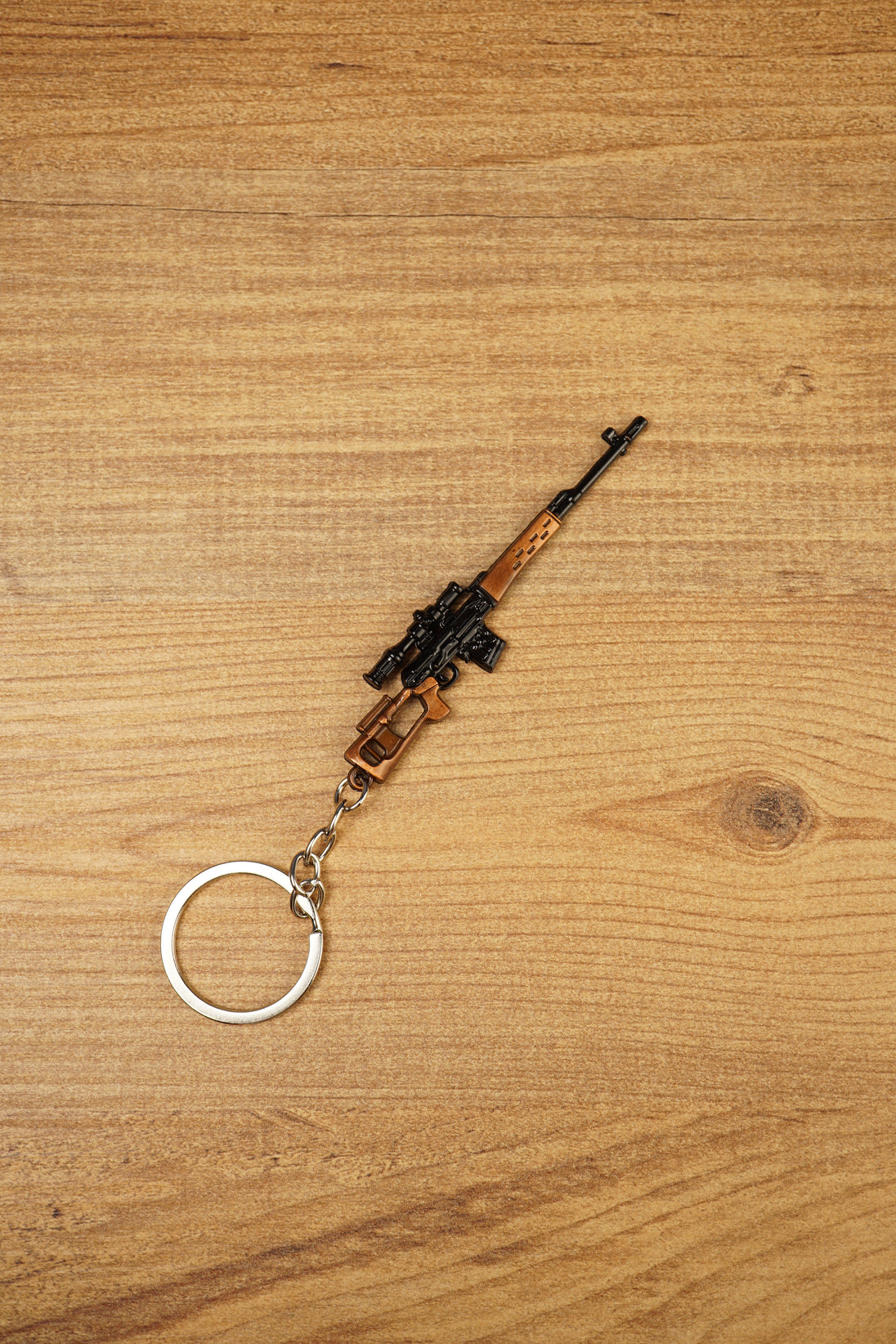 Angled SVDS rifle keychain on wood background with detailed black scope, bronze body and metal keyring for tactical shooter fans