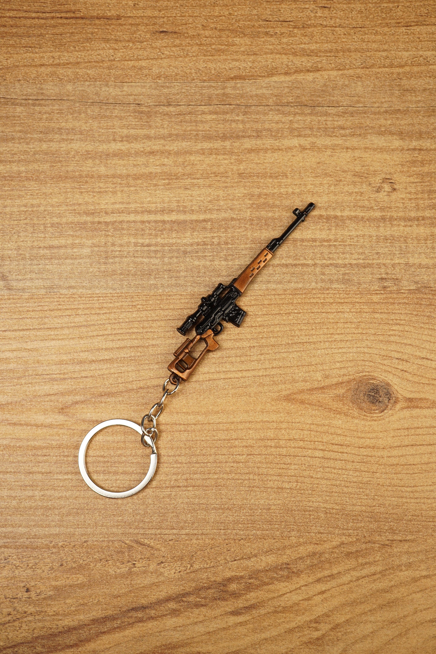 Angled SVDS rifle keychain on wood background with detailed black scope, bronze body and metal keyring for tactical shooter fans