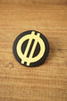 Close-up of a black and yellow Arc Raiders inspired circular pin with raised symbol detail, shown upright on a wooden tabletop.