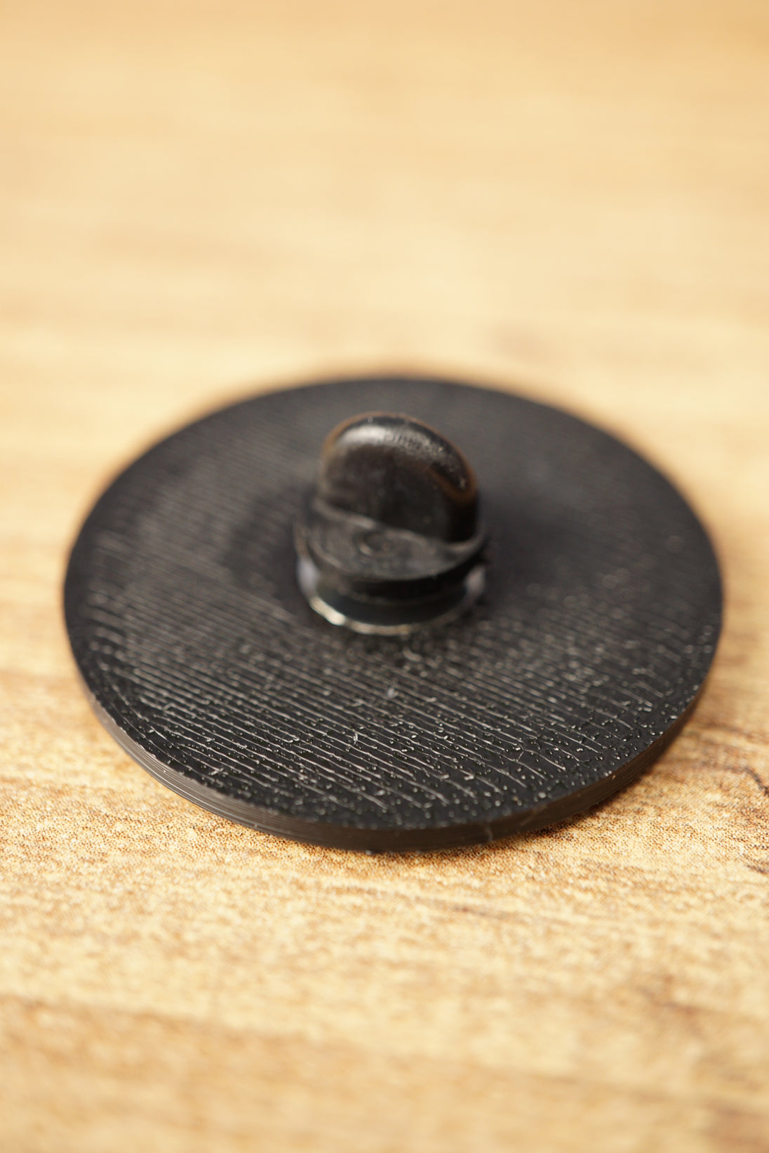 Close-up of the textured black back of an Arc Raiders inspired pin, showing the raised pin clasp and circular accessory design.