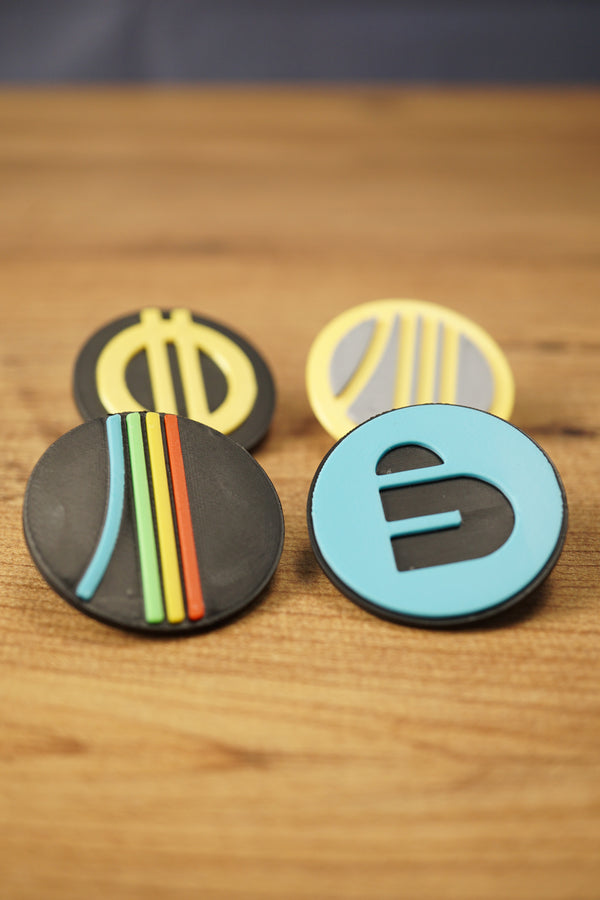 Arc Raiders inspired pin set displayed on a wooden tabletop, featuring four round collectible pins with blue, yellow, grey, black, and multicolor designs.