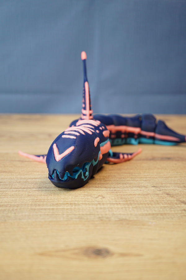 Marrowbreach inspired articulated figure on wooden surface in natural light, showing dark blue body, coral red accents and light blue jaw details.