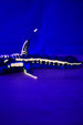 Side view of articulated Marrowbreach creature figure glowing under UV light, showing dark blue body, pale glow markings, fins and segmented tail.