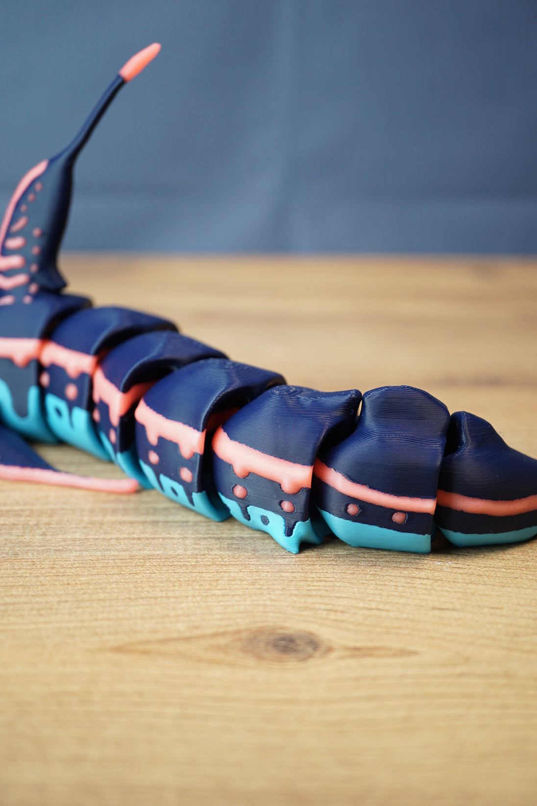 Close side view of the Marrowbreach figure tail section, showing multiple articulated body segments, dark blue shell and coral red side stripe.
