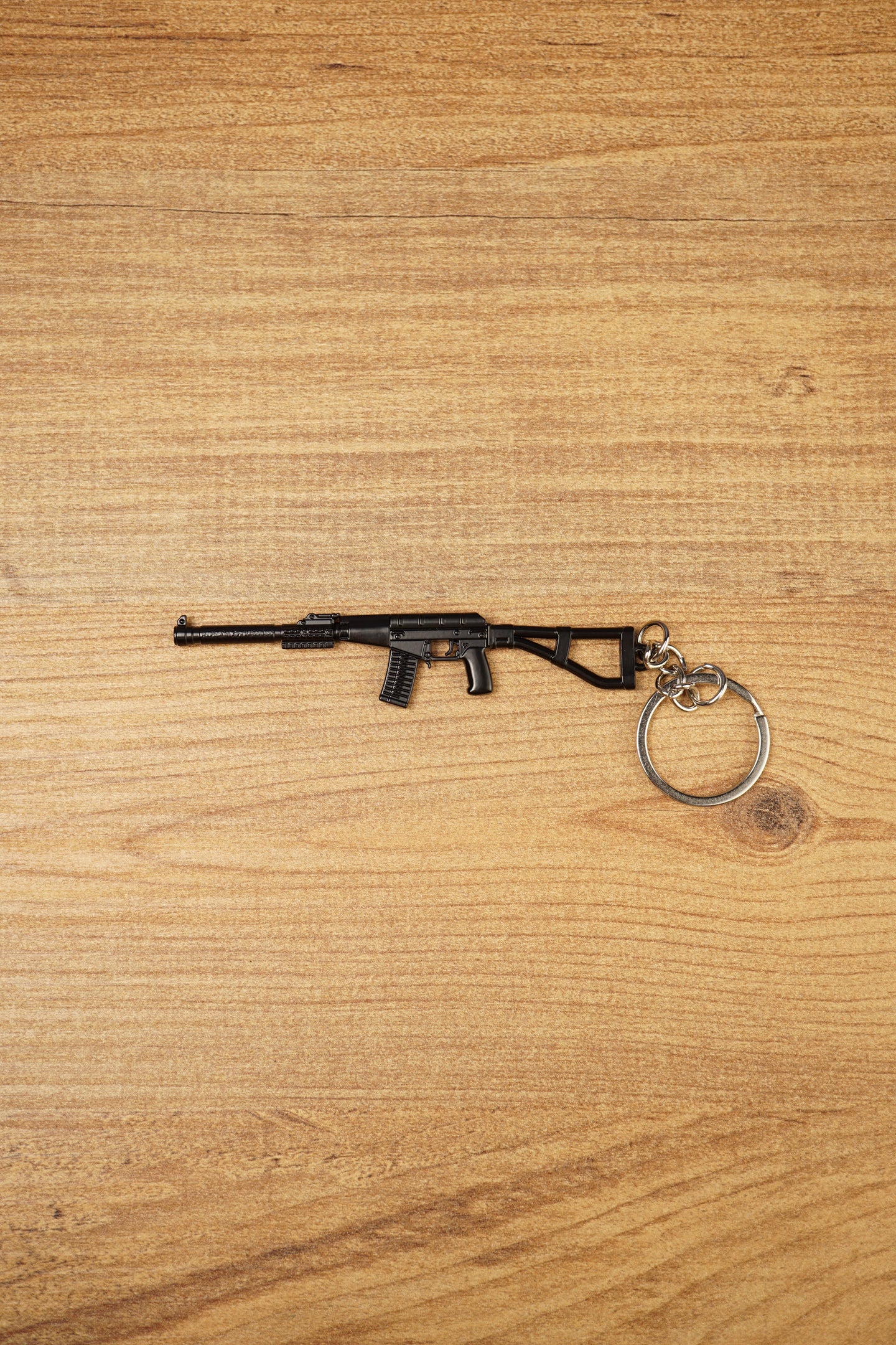 Black AS Val style rifle keychain with long suppressor, compact stock and metal keyring on a wooden tabletop