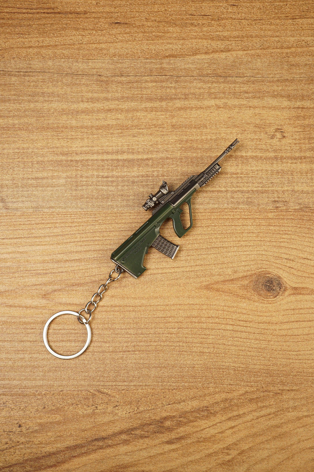 Angled AUG rifle keyring on a wooden background with tactical scope, green stock, metallic barrel and attached silver key ring