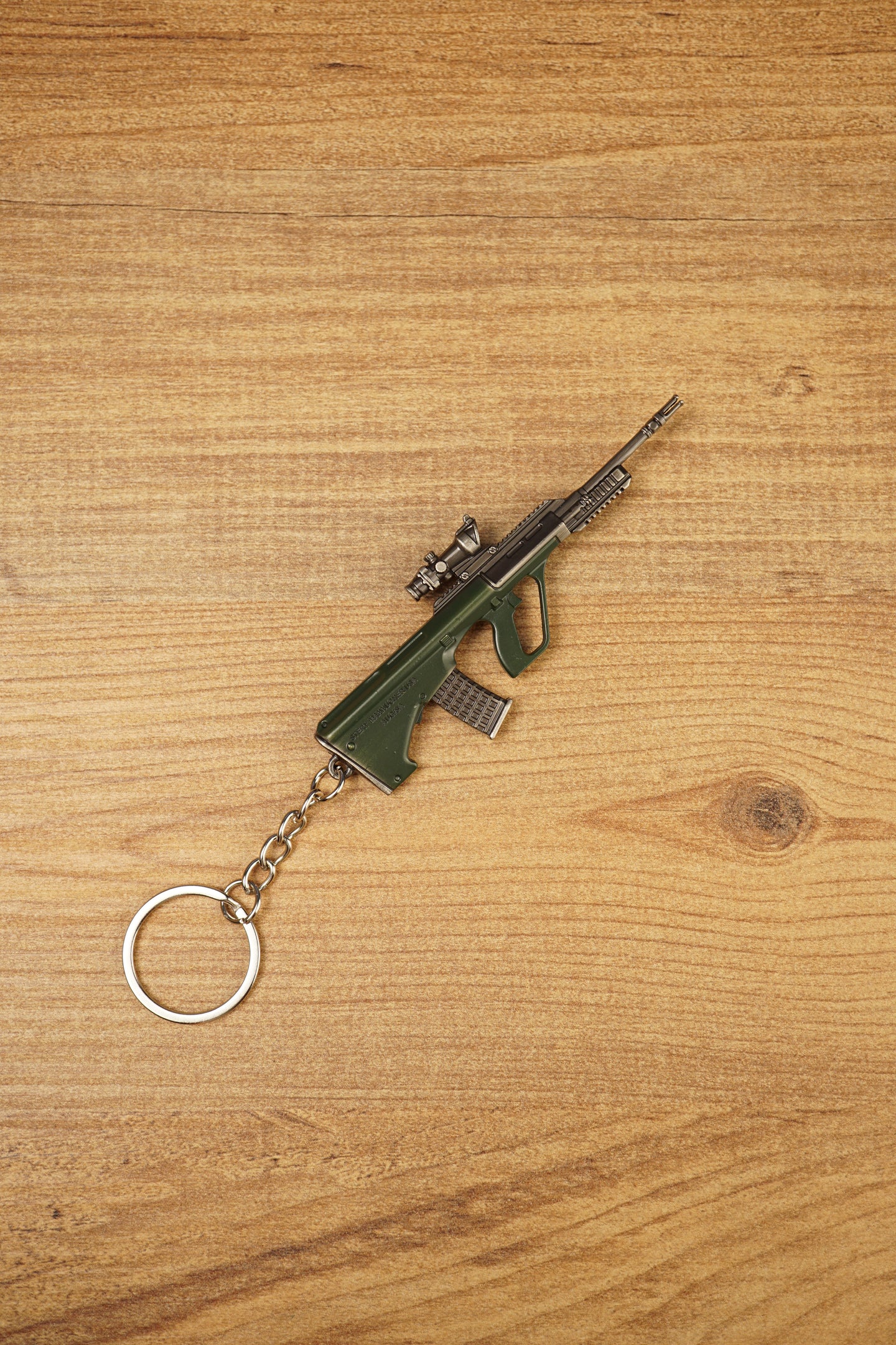 Angled AUG rifle keyring on a wooden background with tactical scope, green stock, metallic barrel and attached silver key ring