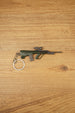 AUG-style metal rifle keyring laid flat on a wooden surface, showing the green bullpup body, scope detail and secure keychain ring