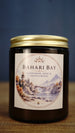 Bahari Bay vegan soy wax candle in an amber glass jar with gold lid, featuring cardamom, rose and sandalwood fragrance notes.