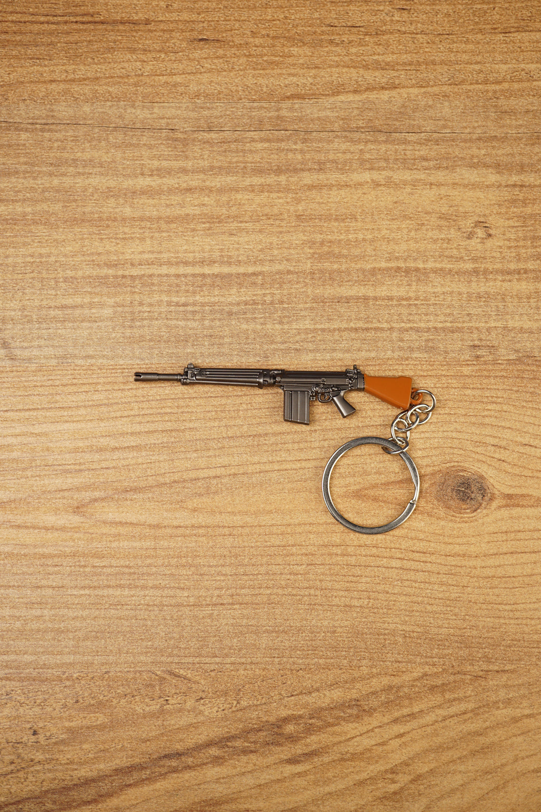 Base SA58 FAL battle rifle keychain with brown stock, metal alloy body and circular keyring shown on a wooden tabletop