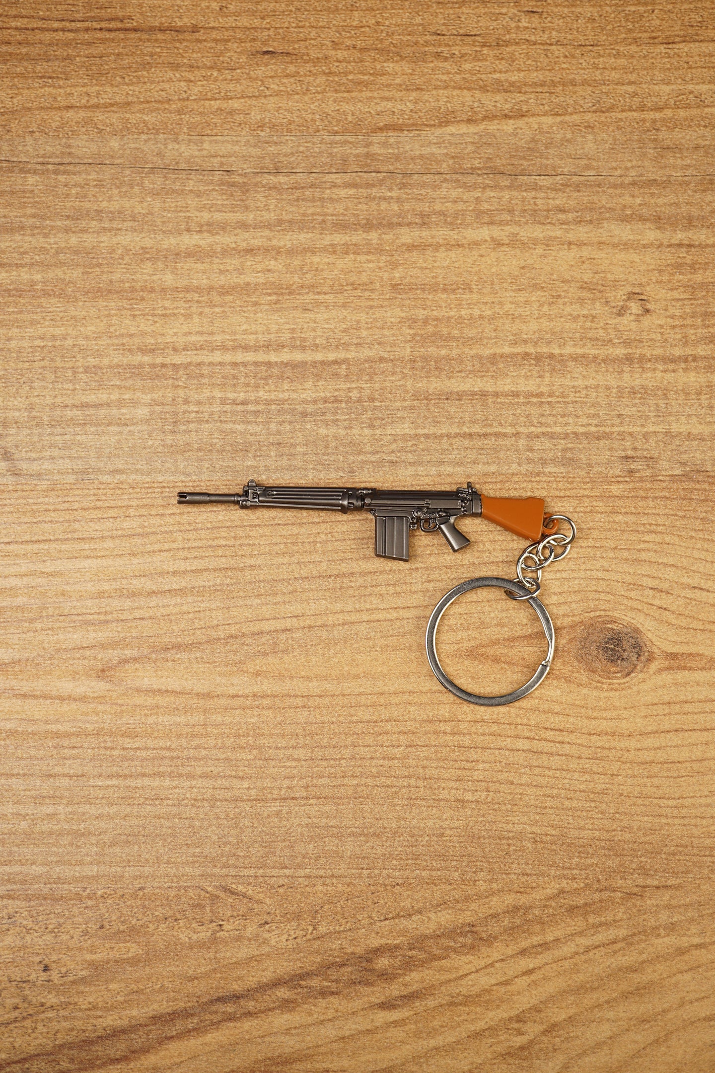 Base SA58 FAL battle rifle keychain with brown stock, metal alloy body and circular keyring shown on a wooden tabletop